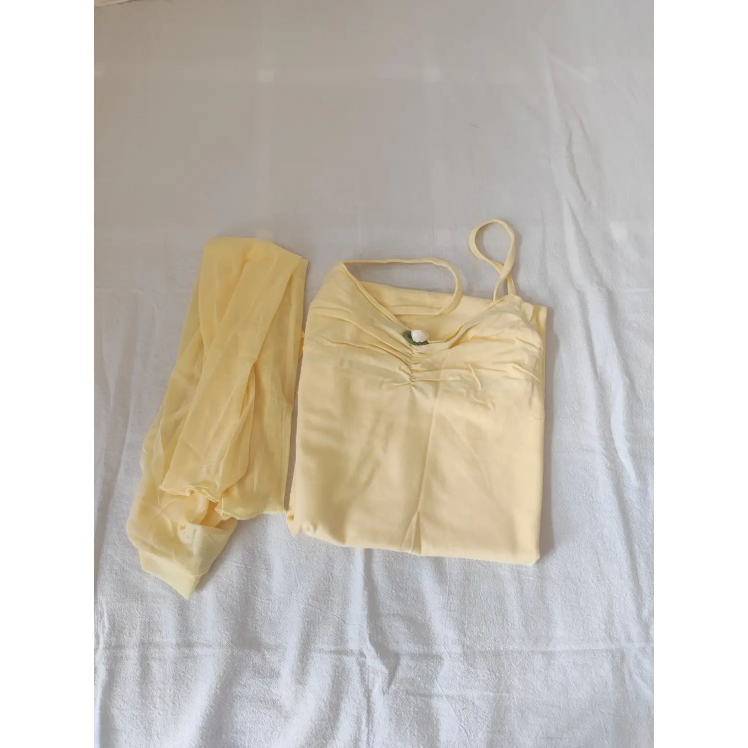 Flat lay folded two piece outfit, pale yellow cami bodycon dress and mesh shrug