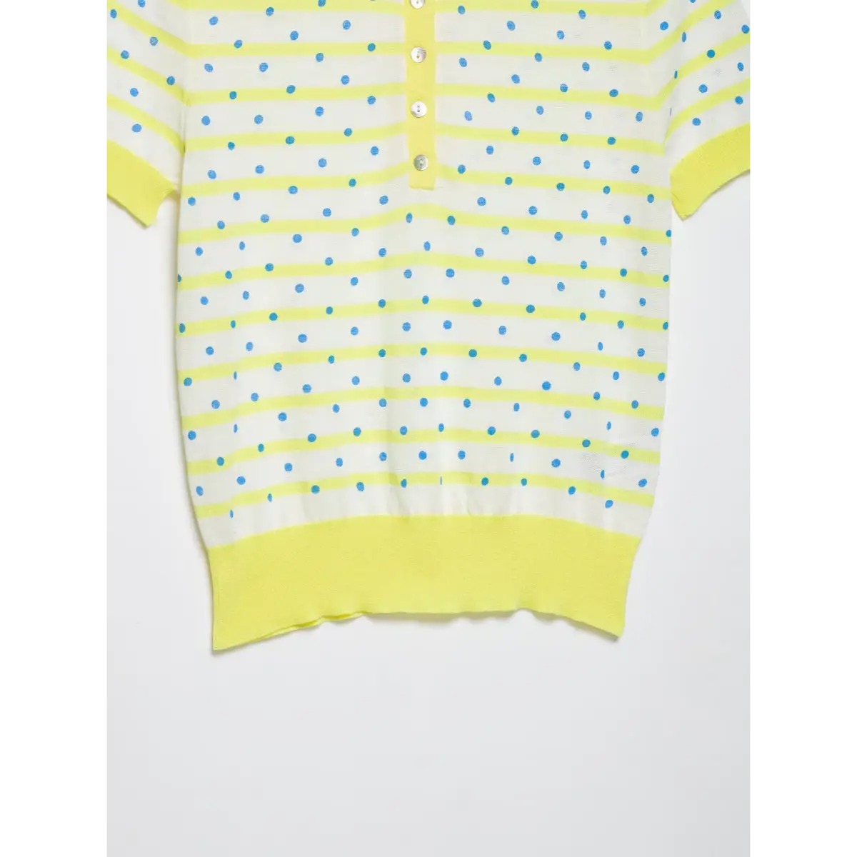 Close-up of the front placket on a yellow and white polka dot knit polo shirt, featuring mother-of-pearl buttons, striped pattern, and ribbed yellow hem/cuffs.