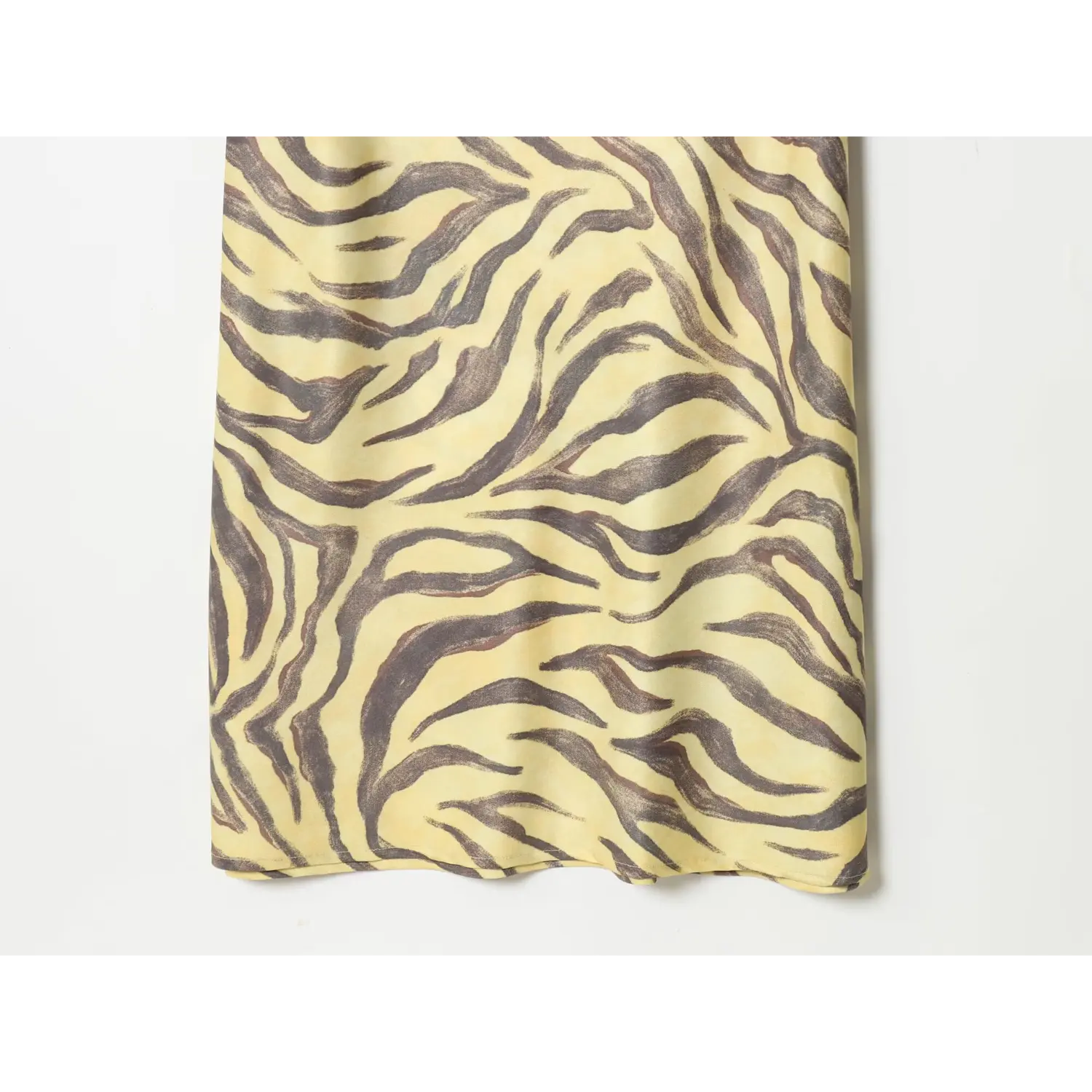 Partial close‑up of midi dress hem, flowing yellow zebra printed satin fabric, clean finished bottom edge