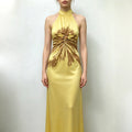 Model wearing yellow satin halter maxi dress, front full body shot, brown abstract floral print, waist twist knot with decorative button