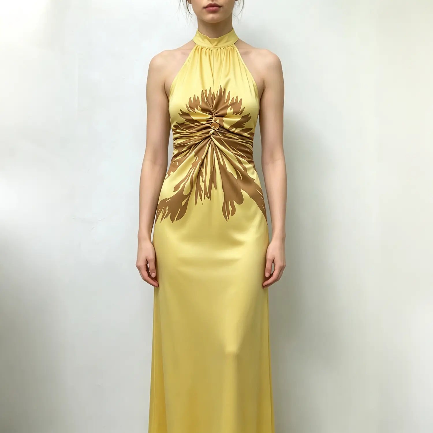 Model wearing yellow satin halter maxi dress, front full body shot, brown abstract floral print, waist twist knot with decorative button