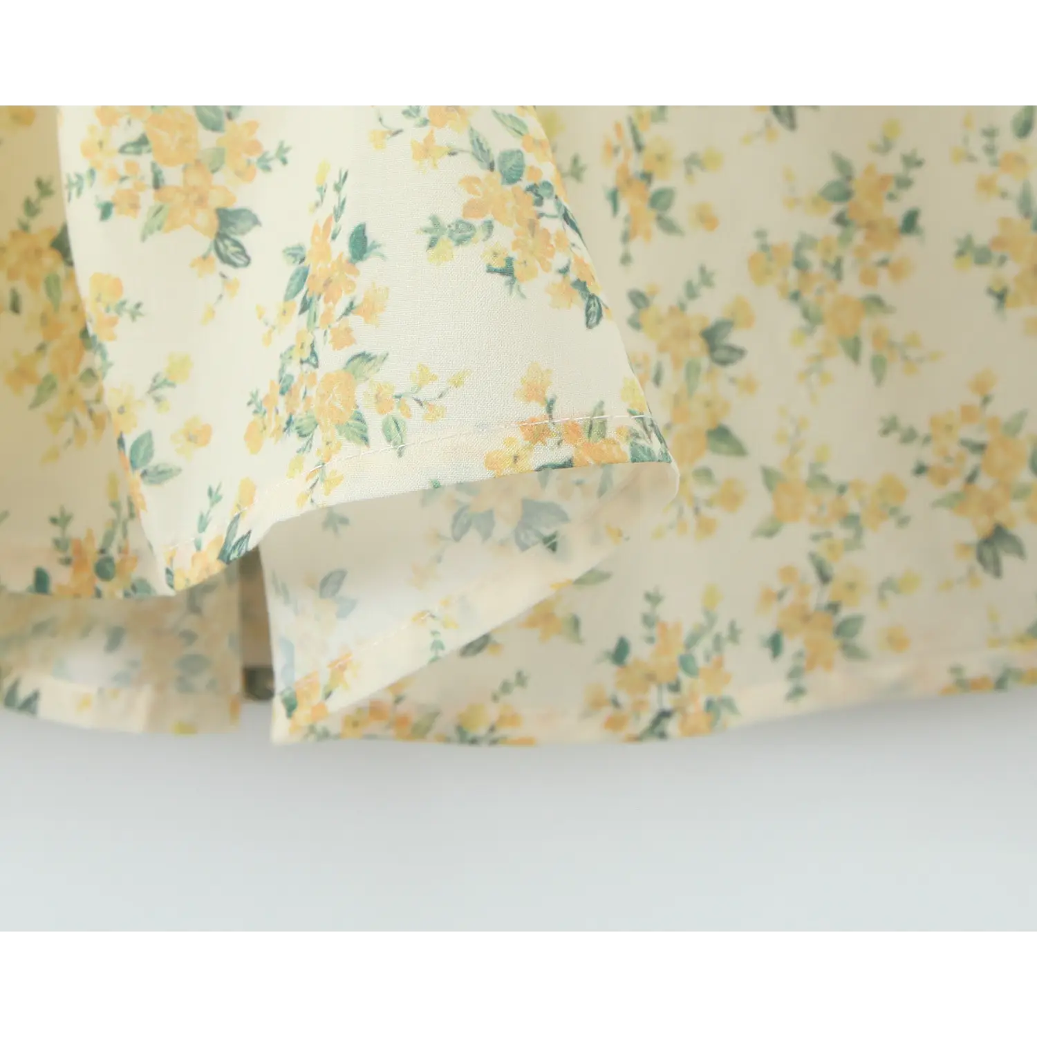 Fabric hem close‑up, neat stitching and yellow green floral print of halter mini dress