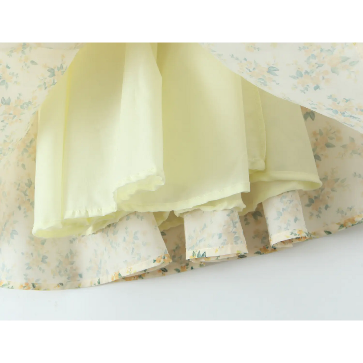 Close‑up shot showing pale yellow inner lining and hem stitching of yellow floral halter mini dress