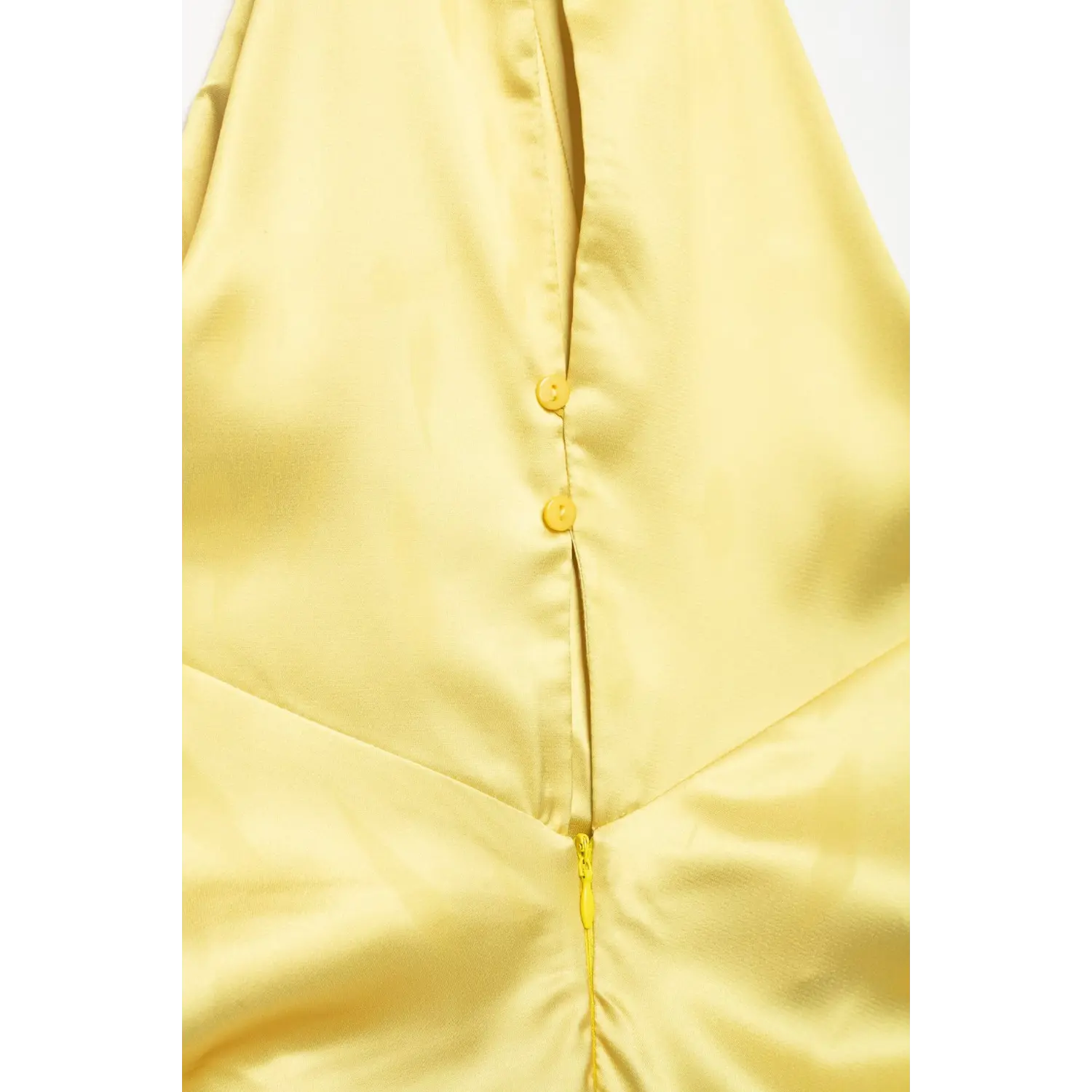 Macro close‑up of yellow halter dress back placket, yellow decorative buttons meeting invisible zipper seam