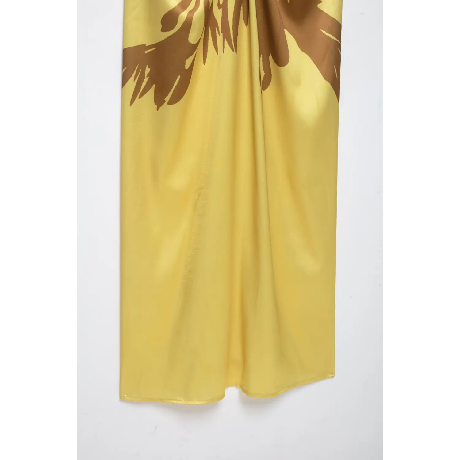 Partial view of yellow satin maxi dress skirt, smooth satin fabric, brown floral print and finished bottom hem