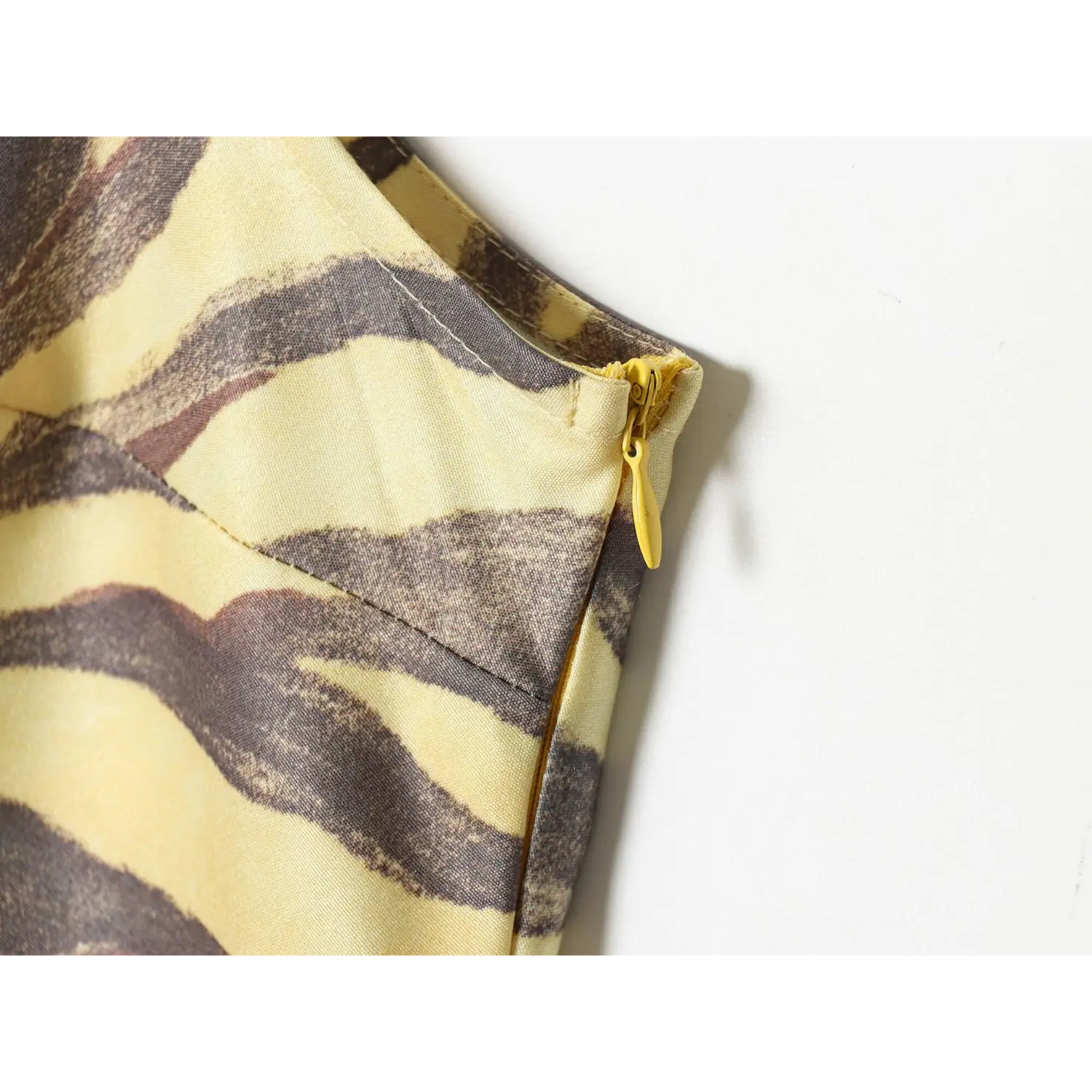 Macro close‑up of side yellow invisible zipper pull on yellow zebra print satin dress, fine fabric weave