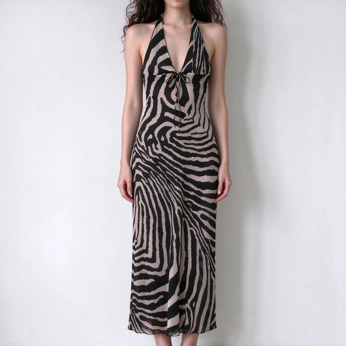 Model wearing zebra print halter maxi dress, deep v neck with front tie, slim fitted silhouette, flowy chiffon fabric, plain white backdrop